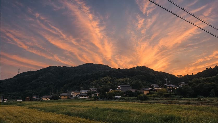 橙色の夕空に包まれる稲田と山里の家々