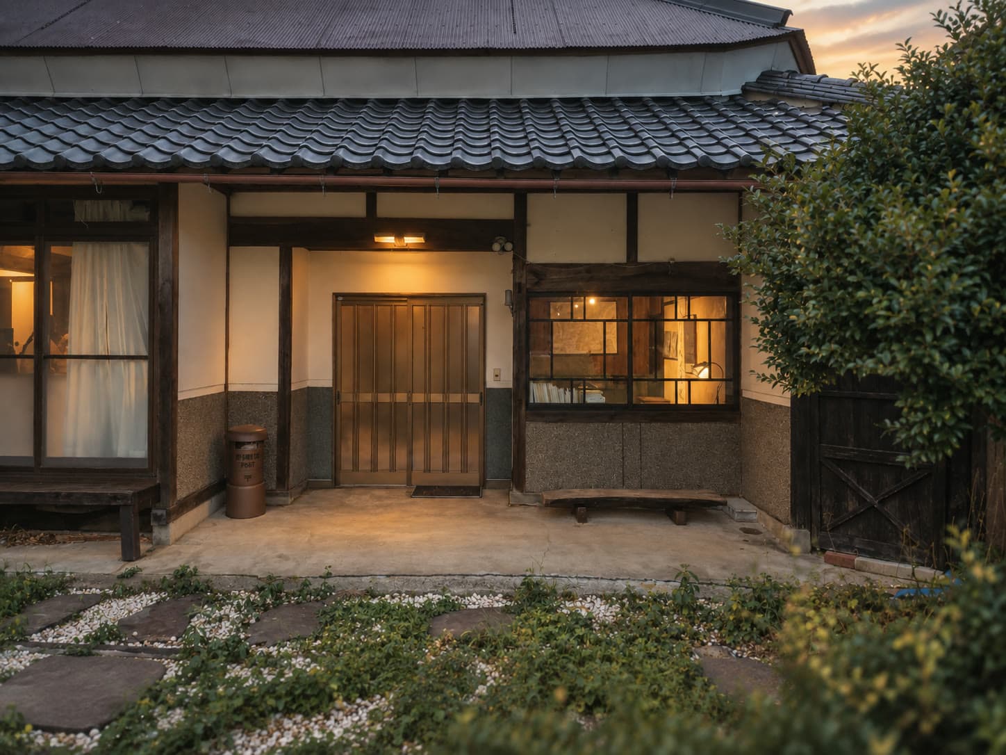 夕暮れ、室内の灯りがともる風山舎の玄関と瓦屋根
