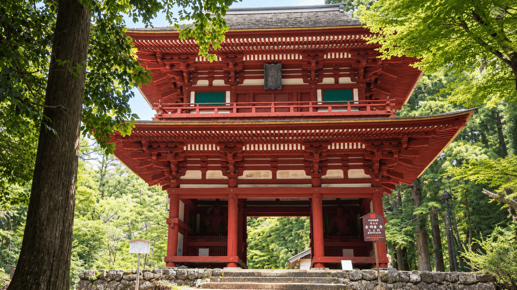 緑の木々に囲まれた鮮やかな朱色の山門