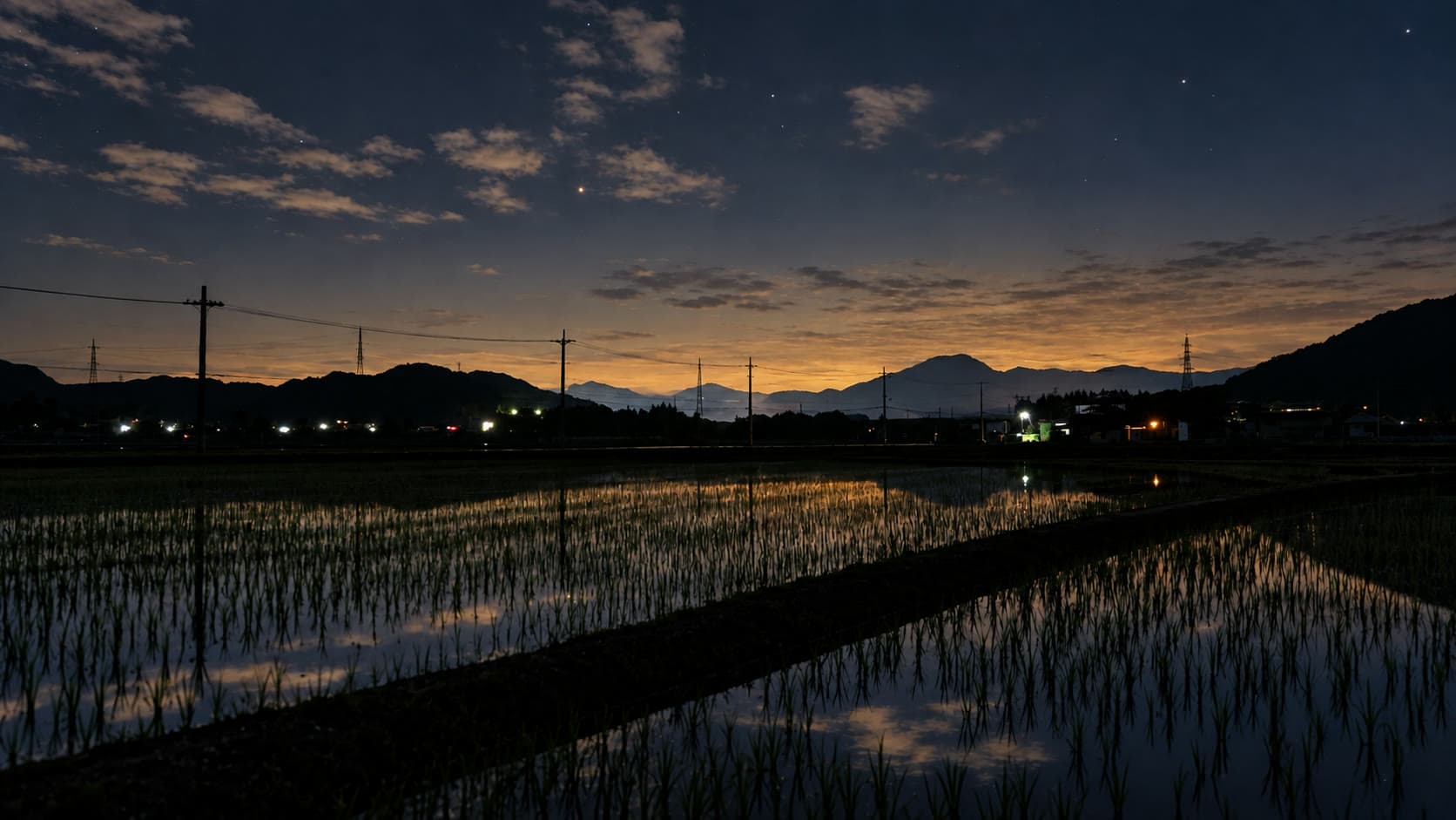 星と夕暮れの光が水田に映る山里の夜